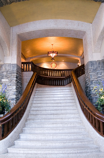 An impressive stairway made of marble with arches and a chandelier at the top. The stairs are in the new lobby of the Firmament Banff Springs Hotel, Banff, Alberta.