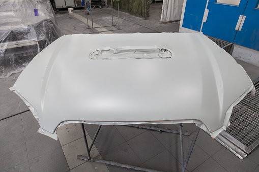 Painting and drying in a professional box of car body parts after applying putty and paint hood in the body repair shop with white lanterns in the working environment.