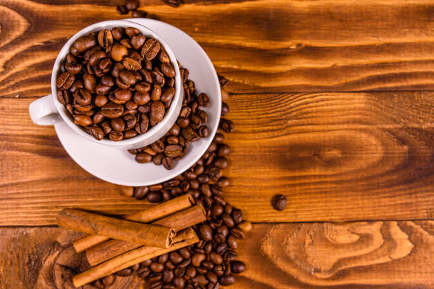 istock White cup filled with coffee beans and cinnamon sticks on wooden table. Top view 1161634888