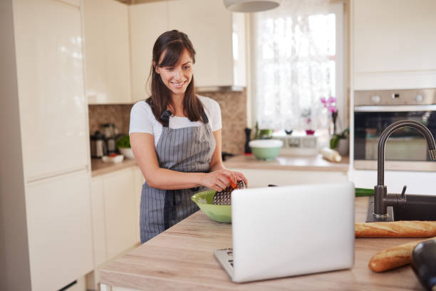 istock Woman preparing dinner while looking at laptop in kitchen. 1161636257