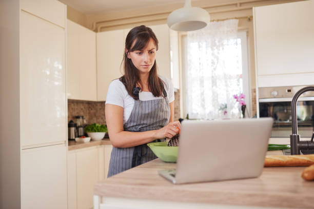 istock Woman preparing dinner while looking at laptop in kitchen. 1161636417