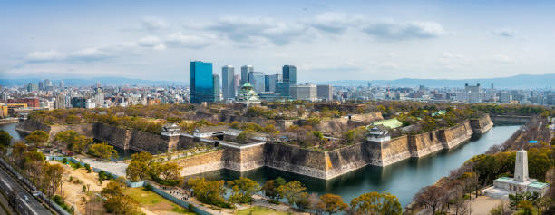 Osaka, Japan - February 26, 2016: The iconic five storey tower of Osaka Castle illuminated by spotlights and reflecting in the tranquil waters of a lake in Osaka Castle Park in the heart of downtown Osaka, Japan's vibrant second city. Panoramic image created from ten contemporaneous sequential photographs.