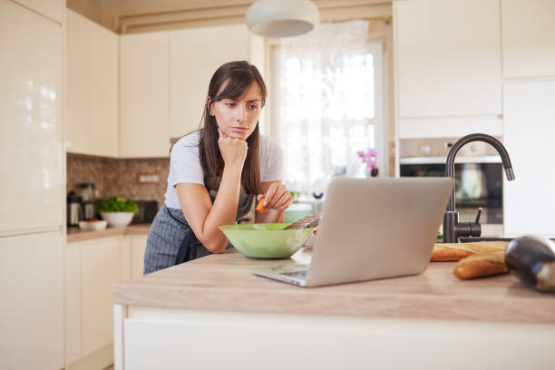 istock Woman preparing dinner in kitchen and looking at laptop. 1161637158