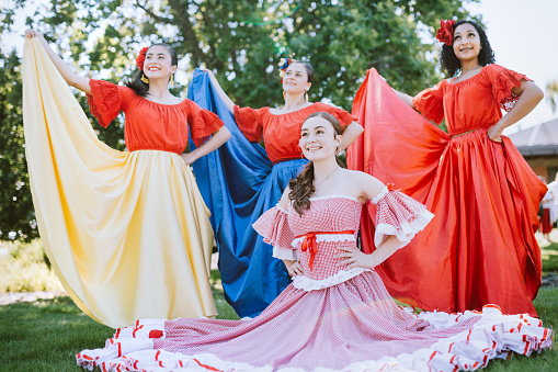 A group of Hispanic girls pose for a picture with their instructor wearing traditional Colombian dance costumes at community event.