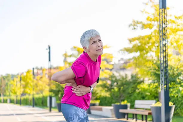 Mature Female Athlete Having an Injury During Exercise Outdoors . Senior woman injury suffering from backache cause of fitness.