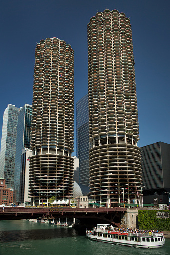 Chicago, Illinois: Vertical frontal view of the Marina City towers by the Chicago River with a tourist cruise sailing under the State St Bridge on a sunny day