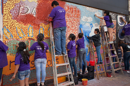Chicago, Illinois: Horizontal shot of a group of students, supervised by their teacher, making a colorful mosaic on a wall of Pilsen Historic District, Lower West Side