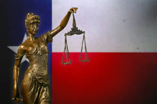 Photo of Lady Justice before a flag of Texas