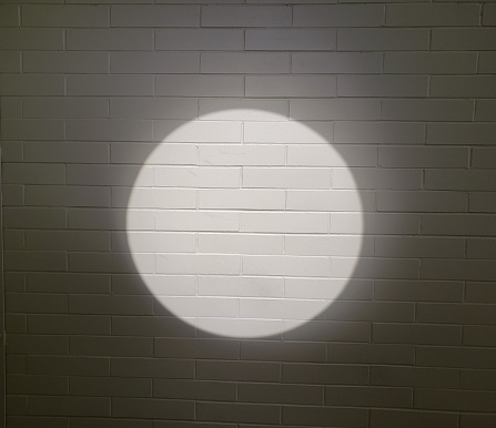 Sunlight coming through a round window creates  a perfect circle on the brick wall inside the building.