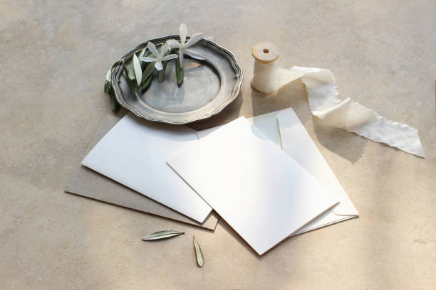istock Summer wedding stationery mock-up scene. Blank greeting cards, envelopes, silver plate with olive branch and white flowers and silk ribbon. Marble background in sunlight, shadows. Top view. 1161649245