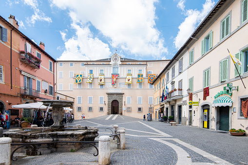 People walking in Piazza della Libertá, a square in front of the Apostolic Palace at the town of Castel Gandolfo, a Roman Castles (Castelli Romani) comune in the Lazio region, Italy. The town is next to the shore of the lake Albano in the volcanic region in Rome province and it holds the Apostolic Palace of Castel Gandolfo which is a summer residence  for the Pope.