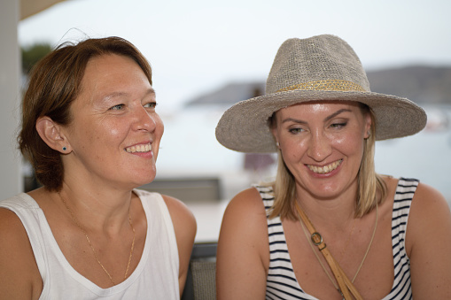Portrait of a two happy women sitting next to the sea and smiling over seaside promenade in summer vacation in a mediterranean village