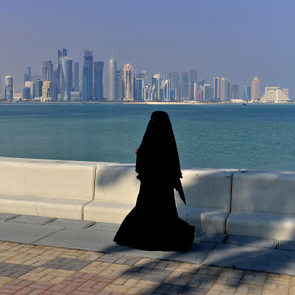 Young woman wearing a burka, taking a walk on the corniche with the iconic Doha skyline in the background on a sunny day in Doha, Qatar