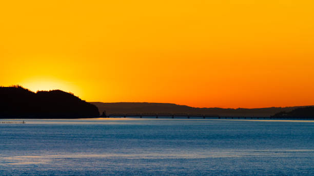 wczesnym rankiem wschód słońca za górami z odbiciem światła słonecznego na oceanie / rzece. sylwetka krajobrazu o świcie, gdy słońce przynosi światło na wybrzeże morskie. - astoria oregon zdjęcia i obrazy z banku zdjęć