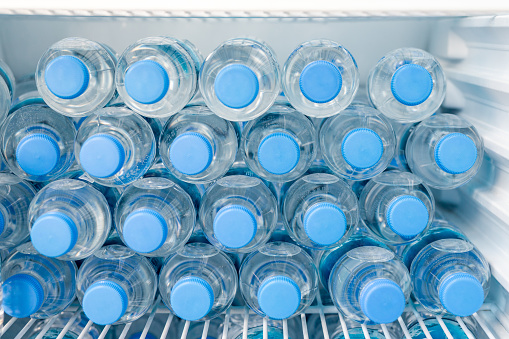 Rows of many transparent plastic bottles with drinking water supply in white refrigerator. Mineral water stack storage in fridge to drink on hot summer day. Healthcare and dehydration prevention.
