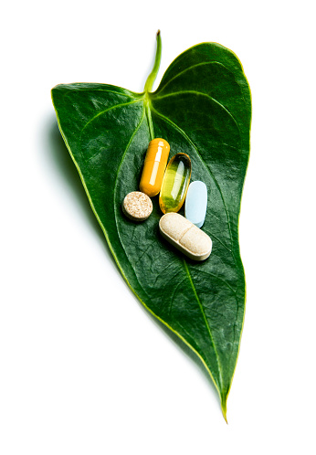 This is a photograph of colorful pills on a green leaf sitting on a white background. There is a clipping path included with this file.