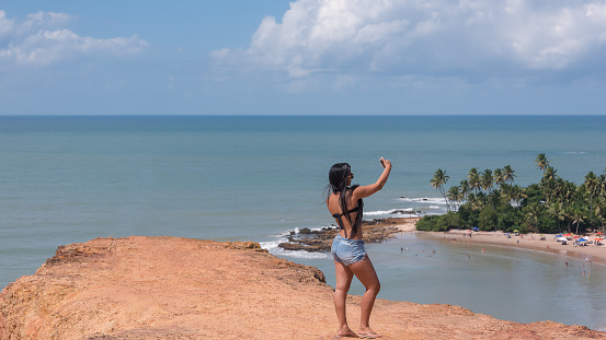 Conde district, Paraíba, Brazil - June 24, 2019:Beautiful young lady takeing picture with her cell phone on the beach