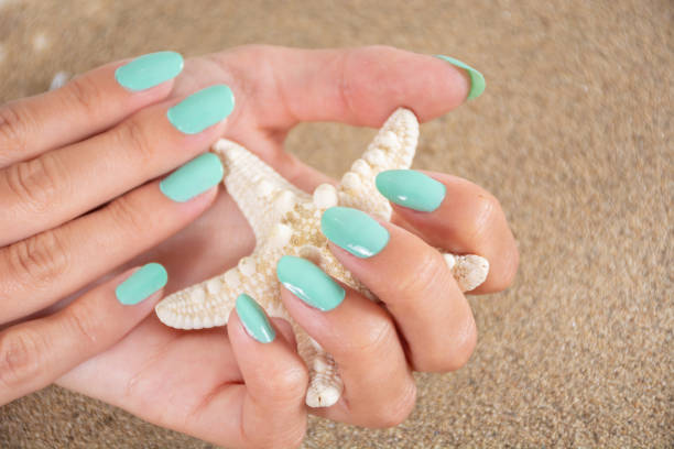 mani da ragazza con un smalto di colore turchese che tiene le stelle marine e la sabbia di mare sullo sfondo - starfish beach white shell foto e immagini stock