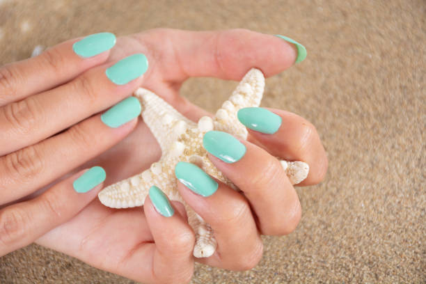 Girl hands with a turquoise color nails polish holding starfish and sea sand in the background Beautiful young girl hands with a turquoise color nails polish holding starfish and sea sand in the background. Manicure and female beauty concept. Close up, selective focus polish beach stock pictures, royalty-free photos & images