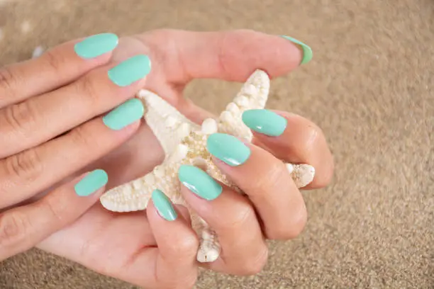 Photo of Girl hands with a turquoise color nails polish holding starfish and sea sand in the background