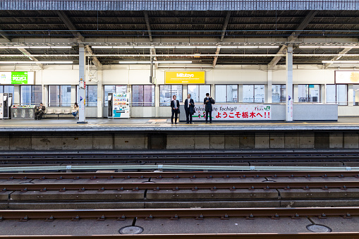 Utsunomiya, Japan - April 4, 2019: Train station platform with business people, businessman waiting for shinkansen bullet train at evening with welcome sign in English to Tochigi