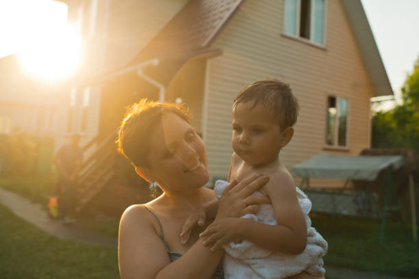 Mother covering little boy with towel after swimming in sunset Family in back yard in the evening vacation rental cleaning stock pictures, royalty-free photos & images