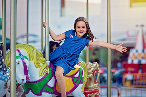 Happy girl is riding horse on carousel