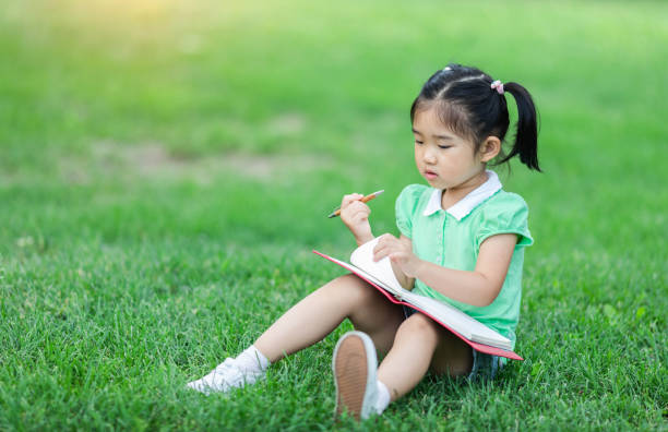 istock Cute Little girl sitting on the grass studying 1161669754