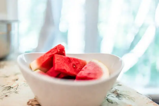 Seedless watermelon fruit red slices in bowl by window on table of house room closeup at dinner party