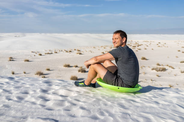 szczęśliwy człowiek siedzący na piasku w białych piaskach wydmy pomnik narodowy w nowym meksyku na zielonym dysku sanki do zsuwania się wzgórza - sliding sands zdjęcia i obrazy z banku zdjęć