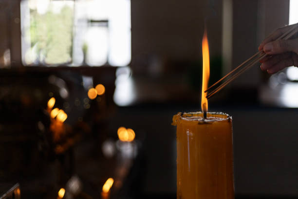 仏教レントコンセプト。仏教寺院の大きなろうそくからお香を巻き上げる女性は、光の形のろうそくを閉じます。低いキースタイルで処理します。テキストまたはデザイン用のコピースペー� - burning temple incense buddhism ストックフォトと画像