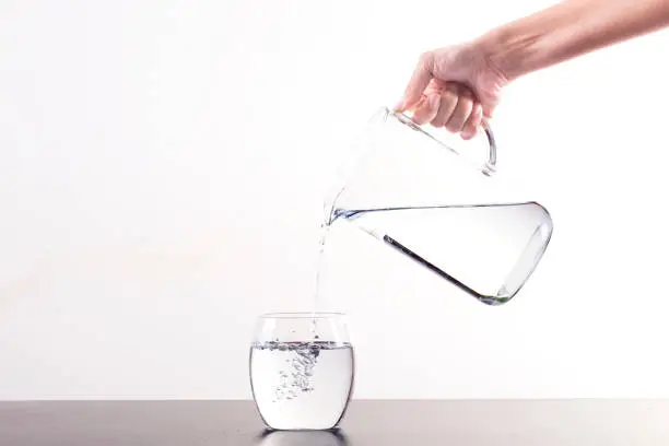 Pouring Water From Pitcher Into Glass, isolated on a white background with copy space