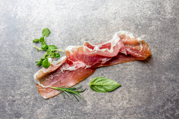 food background with ham jamon serrano and herbs - rosemary, basil and watercress salad, stone gray background, top view - serrano chilli pepper meat ham spain imagens e fotografias de stock