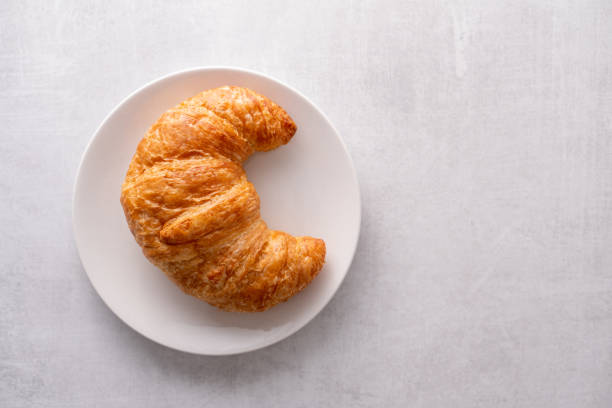 Warm crispy flaky croissant roll on white plate and distressed table stock photo
