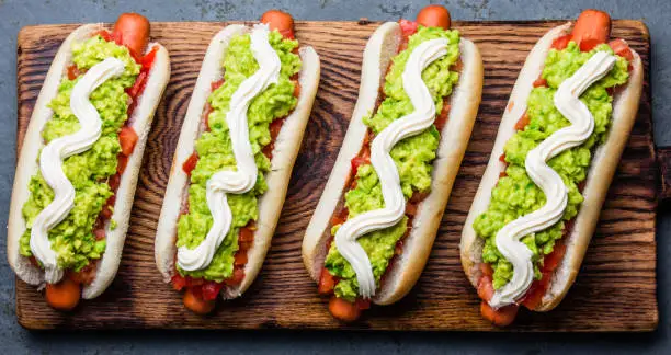 Photo of Chilean Completo Italiano. Hot dog sandwiches with tomato, avocado and mayonnaise on wooden board. Top view.