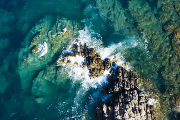 Photo of View from above, stunning aerial view of some waves crashing on a rocky coastline during a windy day in Sardinia, Italy.