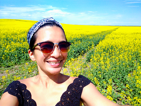 One young adult woman taking a selfie in canola field rural landscape in Alberta, Canada on her travel holiday vacations freedom outdoor lifestyle.