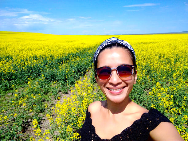 One young adult woman taking a selfie in canola field rural landscape in Alberta, Canada on her travel holiday vacations freedom outdoor lifestyle.