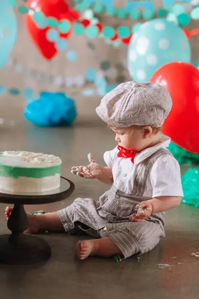Adorable happy baby boy eating cake one at his first birthday cakesmash party.
