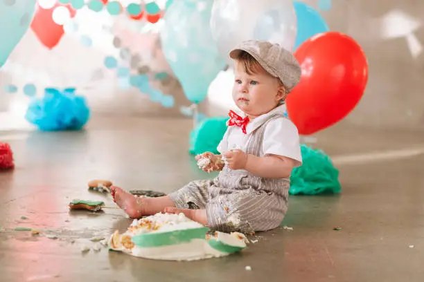 Baby boy touching his first birthday cake. Making messy cakesmash in decorated studio location. Dirty bare foot.