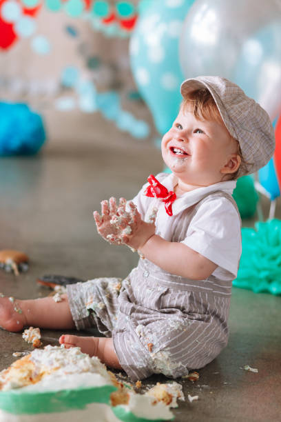 istock Little boy looking side with mouth covered in white icing and cake in decorated studio backdrop. Birthday cakesmash party 1161713332