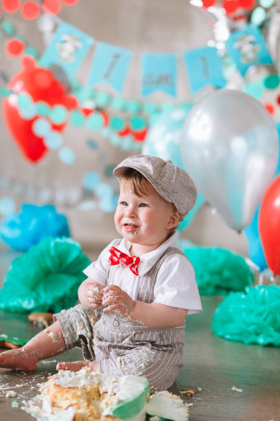 istock Little boy looking side with mouth covered in white icing and cake in decorated studio backdrop. Birthday cakesmash party 1161713346