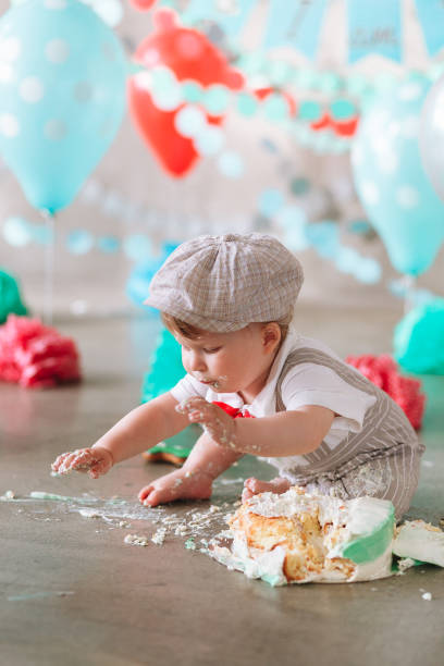 istock Little boy looking side with mouth covered in white icing and cake in decorated studio backdrop. Birthday cakesmash party 1161713425