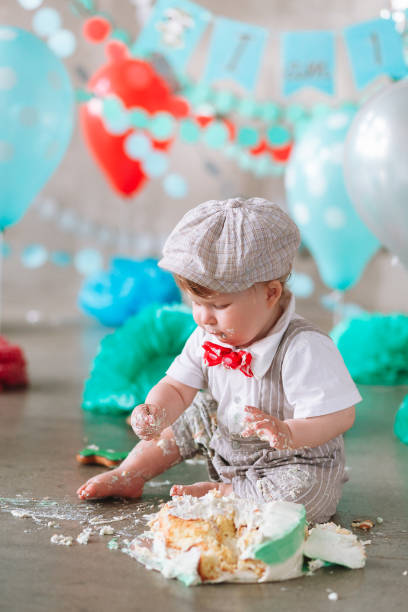istock Little boy looking side with mouth covered in white icing and cake in decorated studio backdrop. Birthday cakesmash party 1161713427