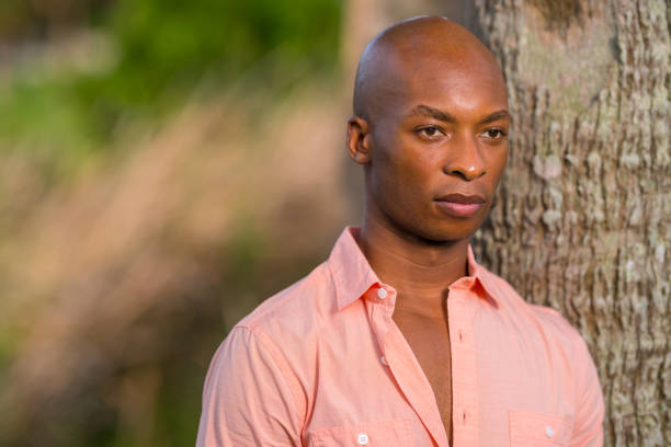 istock Summertime portrait handsome African American man posing by a tree with pink shirt unbuttoned 1161714042