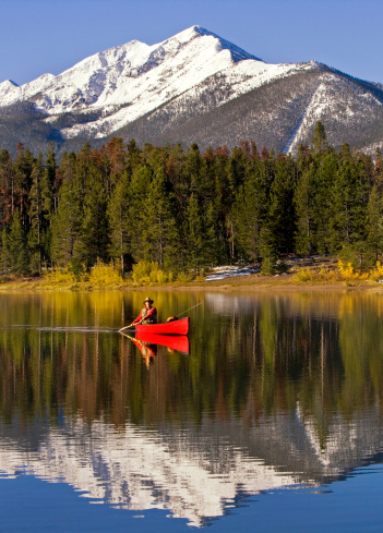 Photo of a man paddling a canoe while fly fishing on Lake Dillon in Summit County, Colorado.