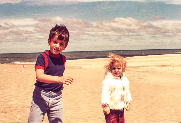 Cold day at the beach Vintage photo of a cute blonde little girl in with her brother at the beach on a cold day. sibling photos stock pictures, royalty-free photos & images