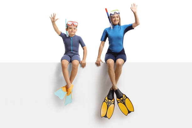 boy and a woman on a panel waving and wearing a wetsuit, a diving mask and diving flippers - child women outdoors mother imagens e fotografias de stock