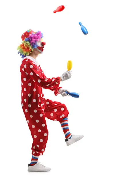 Full length profile shot of a clown juggling with clubs isolated on white background