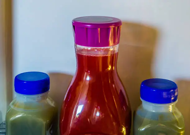 Photo of two green and one red fruit juice in plastic bottles, healthy smoothies in the refrigerator, popular and healthy products